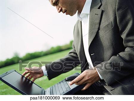 Businessman using laptop computer outdoors, close-up View Large Photo Image Stock Photo - Businessman using laptop computer outdoors, close-up. Fotosearch