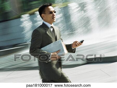 Businessman walking with cell phone in hand, three quarter length, tilt View Large Photo Image Stock Photo - Businessman walking with cell phone in hand, three quarter length, tilt. Fotosearch