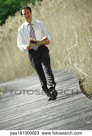 Stock Image - Businessman walking with newspaper in hands, outdoors, portrait. Fotosearch
