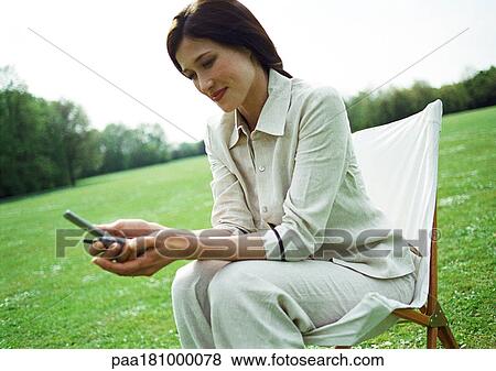 Stock Photo - Businesswoman using cell phone on chair outdoors, close-up. Fotosearch