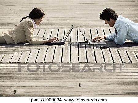 Man and woman lying on stomachs, outdoors, with laptop computers View Large Photo Image Picture - Man and woman lying on stomachs, outdoors, with laptop computers. Fotosearch
