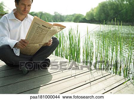 Picture - Man sitting outdoors, reading newspaper. Fotosearch