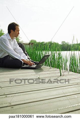 Man sitting outdoors with laptop computer View Large Photo Image Stock Image - Man sitting outdoors with laptop computer. Fotosearch