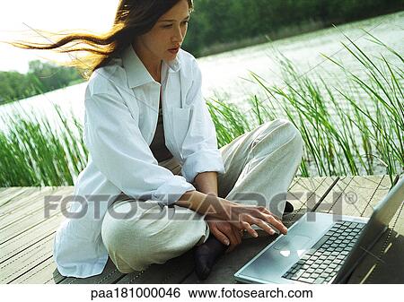 Woman sitting outdoors, using laptop computer View Large Photo Image Stock Photograph - Woman sitting outdoors, using laptop computer. Fotosearch