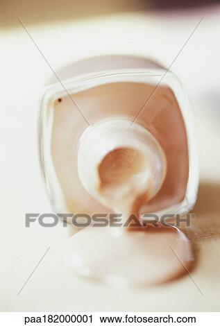 Stock Image - Foundation spilling out of bottle, close-up. Fotosearch