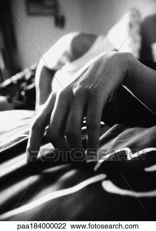 Stock Image - Hand of person lying on bed, close-up, b&w. Fotosearch