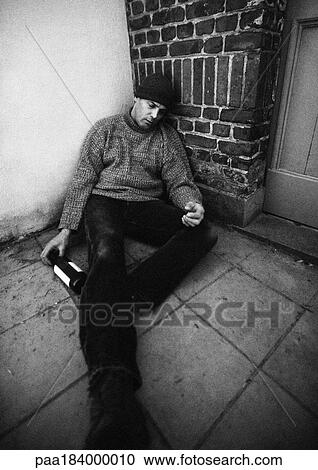 Stock Image - Man sitting on ground with bottle in hand and eyes closed. Fotosearch