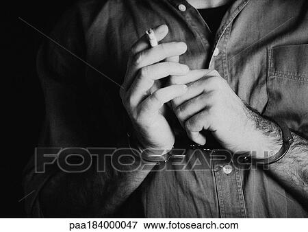 Stock Photo - Man wearing handcuffs and holding cigarette, close-up, b&w. Fotosearch