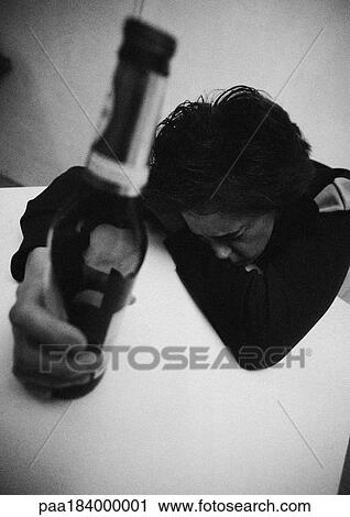 Woman holding bottle, leaning head on table, b&w View Large Photo Image Stock Image - Woman holding bottle, leaning head on table, b&w. Fotosearch
