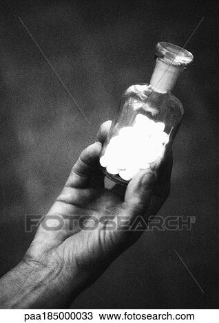 Stock Image - Hand holding bottle of pills, close-up, b&w. Fotosearch
