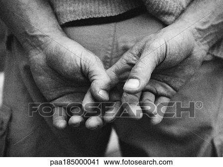 Stock Image - Hands together behind back, close-up, b&w. Fotosearch
