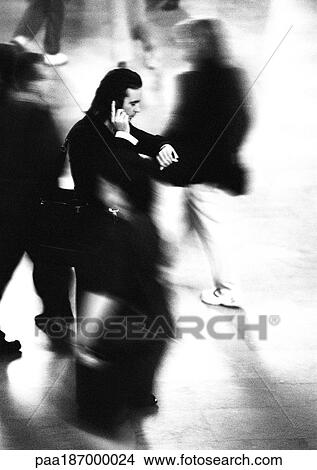 Businessman standing and using cell phone in crowd, blurred motion, b&w View Large Photo Image Picture - Businessman standing and using cell phone in crowd, blurred motion, b&w. Fotosearch