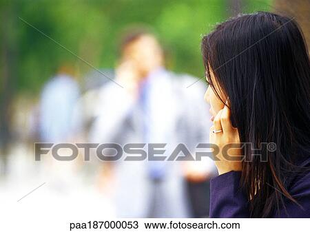Stock Image - Businesswoman using cell phone, close-up, blurred background. Fotosearch