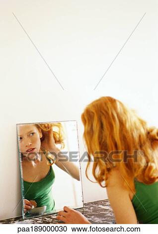 Woman looking at reflection in mirror, pulling her hair back. View Large Photo Image Stock Image - Woman looking at reflection in mirror, pulling her hair back.. Fotosearch