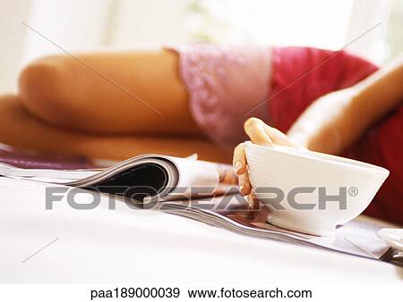 Woman lying on bed, mid-section, blurred, with magazine and bowl in focus in foreground, close-up. View Large Photo Image Stock Photo - Woman lying on bed, mid-section, blurred, with magazine and bowl in focus in foreground, close-up.. Fotosearch