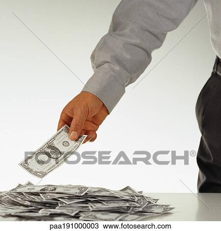 Stock Image - Man holding a dollar over a pile of money.. Fotosearch