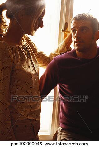 Stock Photography - Man and woman standing in front of window, looking at each other. Fotosearch