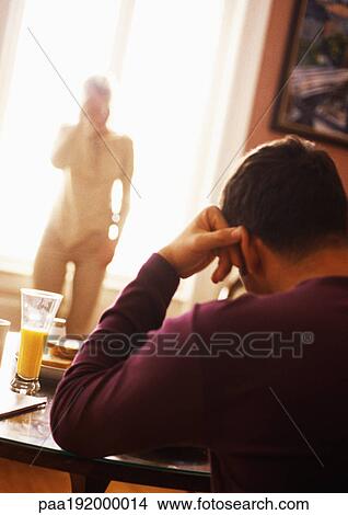 Picture - Man sitting at table, rear view, in focus, woman standing in background, blurred.. Fotosearch