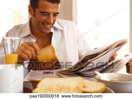 Stock Photo - Man sitting reading newspaper, eating breakfast.. Fotosearch