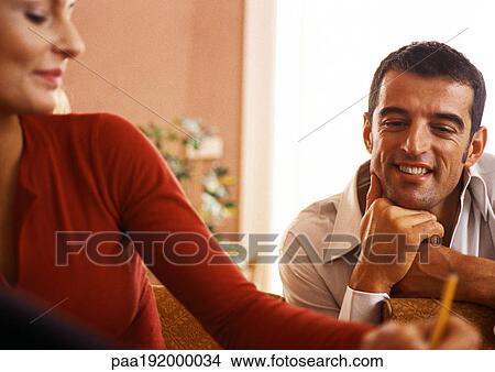 Picture - Man smiling, watching woman write. Fotosearch