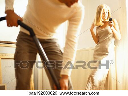 Man vacuuming, woman dialing cell phone in background. View Large Photo Image Stock Photograph - Man vacuuming, woman dialing cell phone in background.. Fotosearch