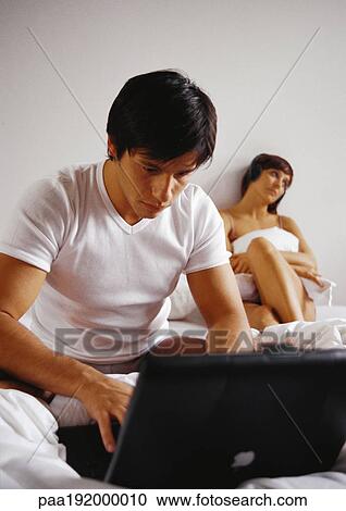 Man working on laptop computer in bed, woman in background. View Large Photo Image Stock Image - Man working on laptop computer in bed, woman in background.. Fotosearch