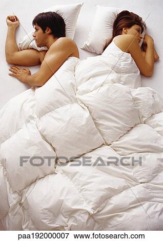 Stock Photo - Woman and man lying in bed, facing opposite directions, high angle view. Fotosearch