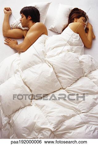 Stock Photograph - Woman and man lying in bed, facing opposite directions, high angle view. Fotosearch
