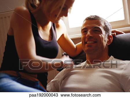 Stock Image - Woman looking down at man in chair, laughing.. Fotosearch