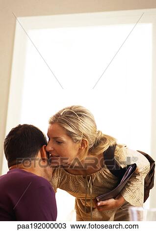 Stock Image - Woman whispering into man's ear.. Fotosearch