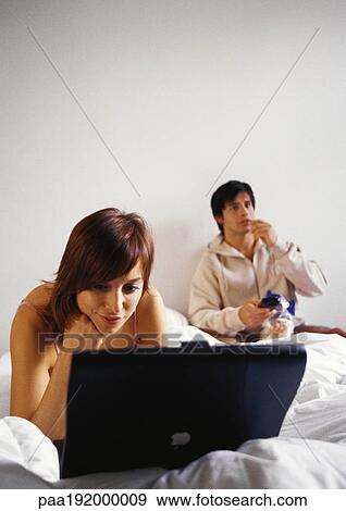 Stock Photo - Woman working on laptop computer in bed, man eating.. Fotosearch