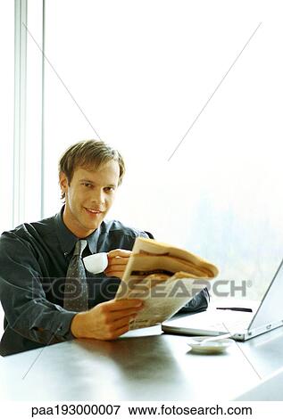 Businessman sitting at desk, drinking and reading. View Large Photo Image Stock Photo - Businessman sitting at desk, drinking and reading.. Fotosearch