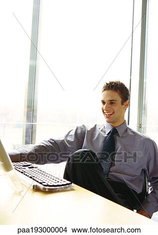 Businessman sitting at desk smiling. View Large Photo Image Picture - Businessman sitting at desk smiling.. Fotosearch