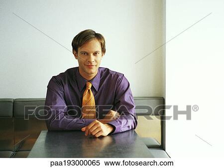 Businessman sitting at table, smiling at camera View Large Photo Image Stock Photography - Businessman sitting at table, smiling at camera. Fotosearch