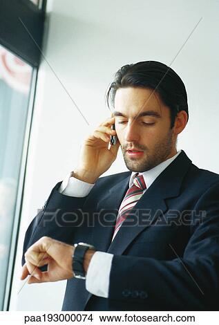 Picture - Businessman talking on cell phone, looking at watch.. Fotosearch