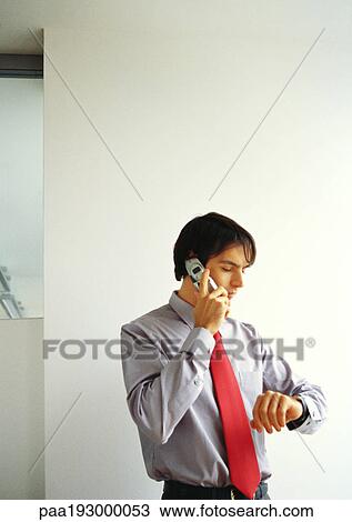 Businessman talking on cell phone, looking down at watch. View Large Photo Image Stock Image - Businessman talking on cell phone, looking down at watch.. Fotosearch
