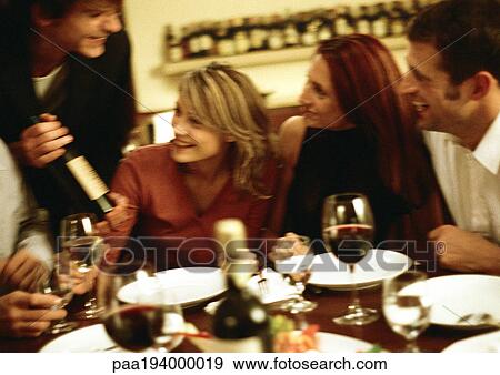 Group of young people around table, one man showing wine View Large Photo Image Stock Photo - Group of young people around table, one man showing wine. Fotosearch