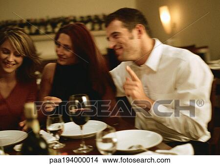 Group of young people sitting at table, having dinner together View Large Photo Image Picture - Group of young people sitting at table, having dinner together. Fotosearch