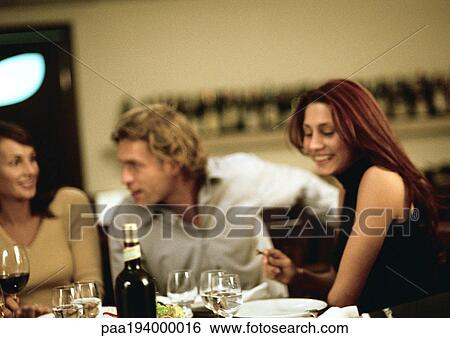 Group of young people sitting at table, having dinner together View Large Photo Image Stock Photograph - Group of young people sitting at table, having dinner together. Fotosearch