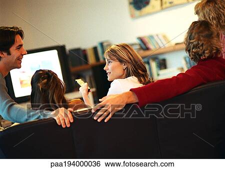 Stock Photograph - People sitting on couch, talking and watching tv, rear view. Fotosearch