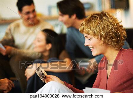 Woman looking at photo, group of people sitting, talking in background View Large Photo Image Stock Photo - Woman looking at photo, group of people sitting, talking in background. Fotosearch