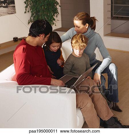 Family sitting together on sofa, looking at laptop. View Large Photo Image Stock Image - Family sitting together on sofa, looking at laptop.. Fotosearch