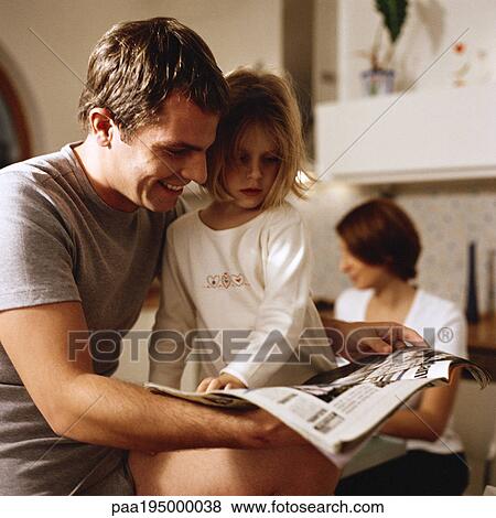 Father sitting with daughter looking at paper, woman in background View Large Photo Image Stock Photo - Father sitting with daughter looking at paper, woman in background. Fotosearch