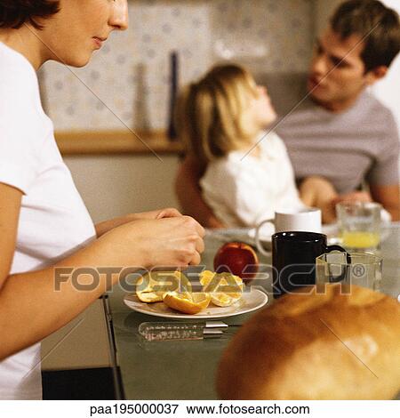 Stock Photo - Mother peeling orange, daughter sitting on father's lap. Fotosearch