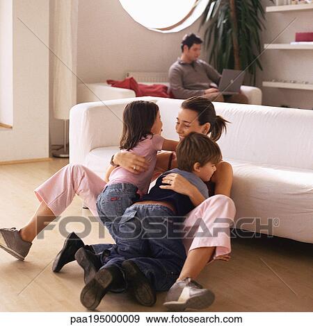 Woman being hugged by two children, man working on laptop in background View Large Photo Image Stock Photo - Woman being hugged by two children, man working on laptop in background. Fotosearch