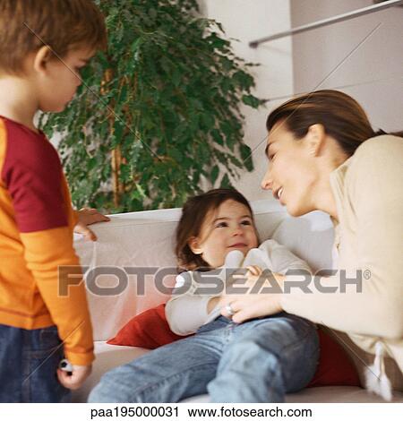 Woman holding daughter on couch, son standing nearby. View Large Photo Image Stock Image - Woman holding daughter on couch, son standing nearby.. Fotosearch