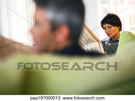 Stock Image - Businessman and businesswoman reading newspaper, blurred foreground.. Fotosearch