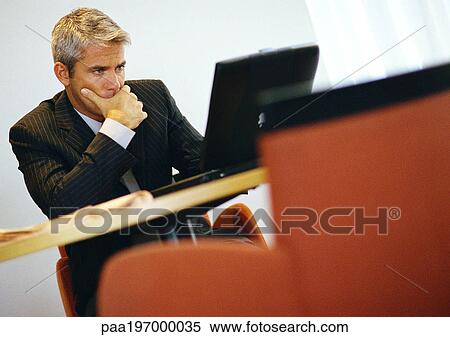 Stock Photography - Businessman, hand to chin, working on computer.. Fotosearch
