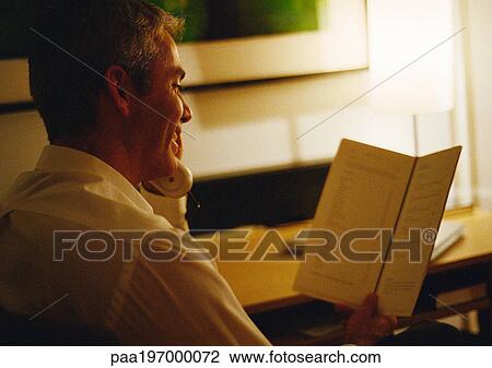 Businessman on phone looking at room service menu View Large Photo Image Stock Image - Businessman on phone looking at room service menu. Fotosearch