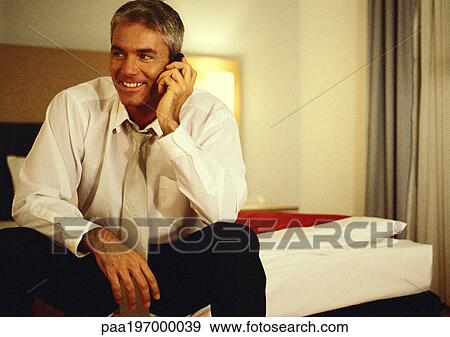 Businessman sitting on bed, talking on cell phone. View Large Photo Image Stock Photo - Businessman sitting on bed, talking on cell phone.. Fotosearch